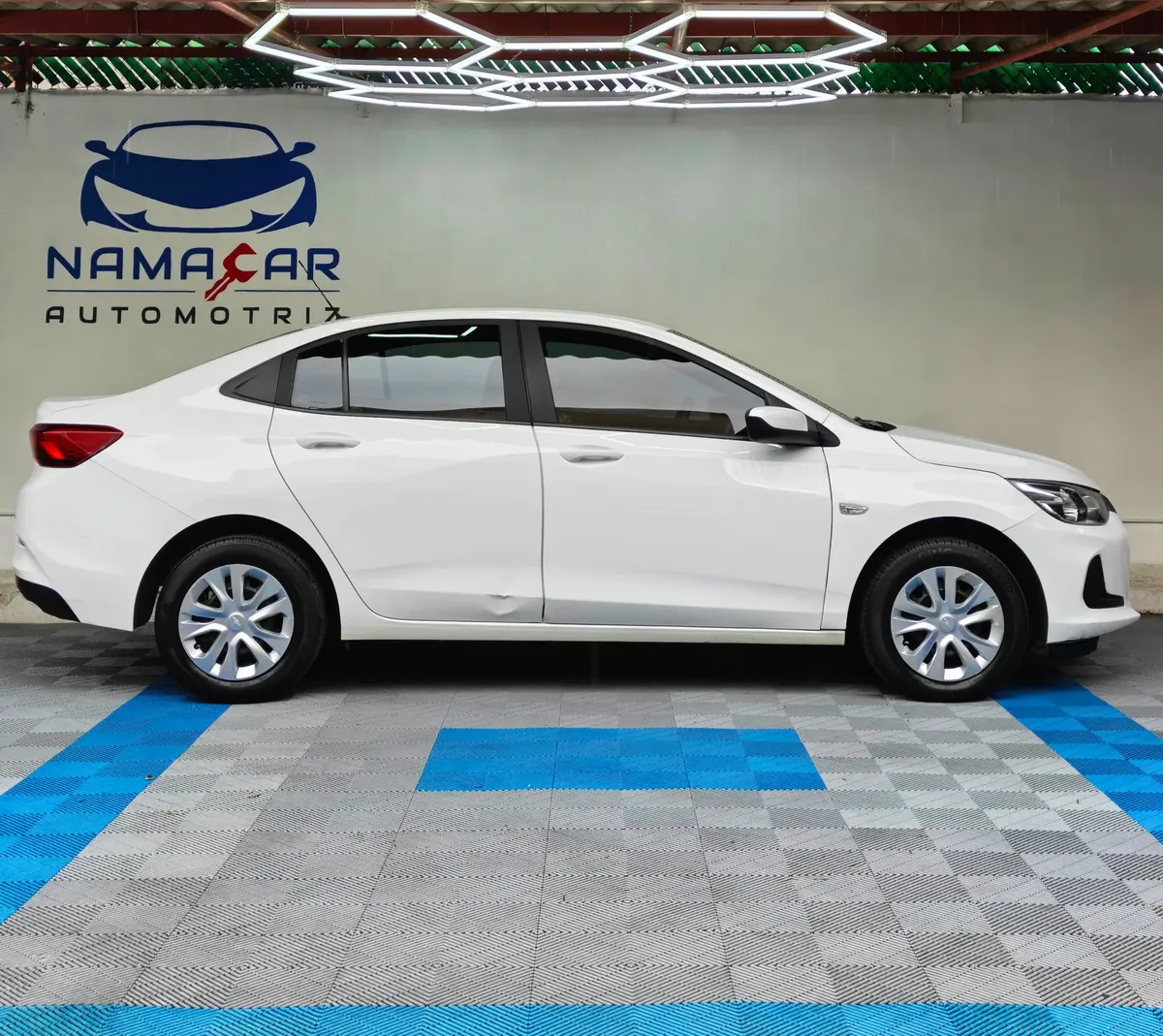 Auto sedán Chevrolet Onix 1.3 LS manual año 2024 seminuevo en color blanco, vista exterior lateral perfil derecho completo exhibido en Namacar Automotriz.